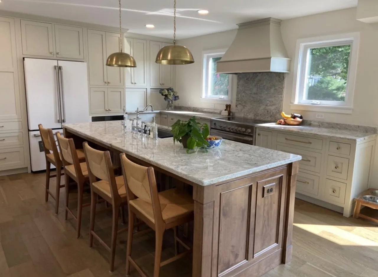 Custom kitchen cabinetry with granite island, brass pendants and a plaster range hood