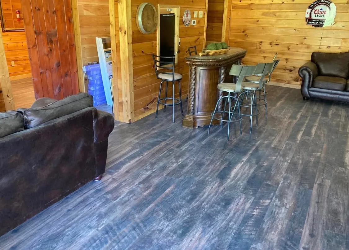 Luxury vinyl plank flooring installed in a wood-paneled basement bar