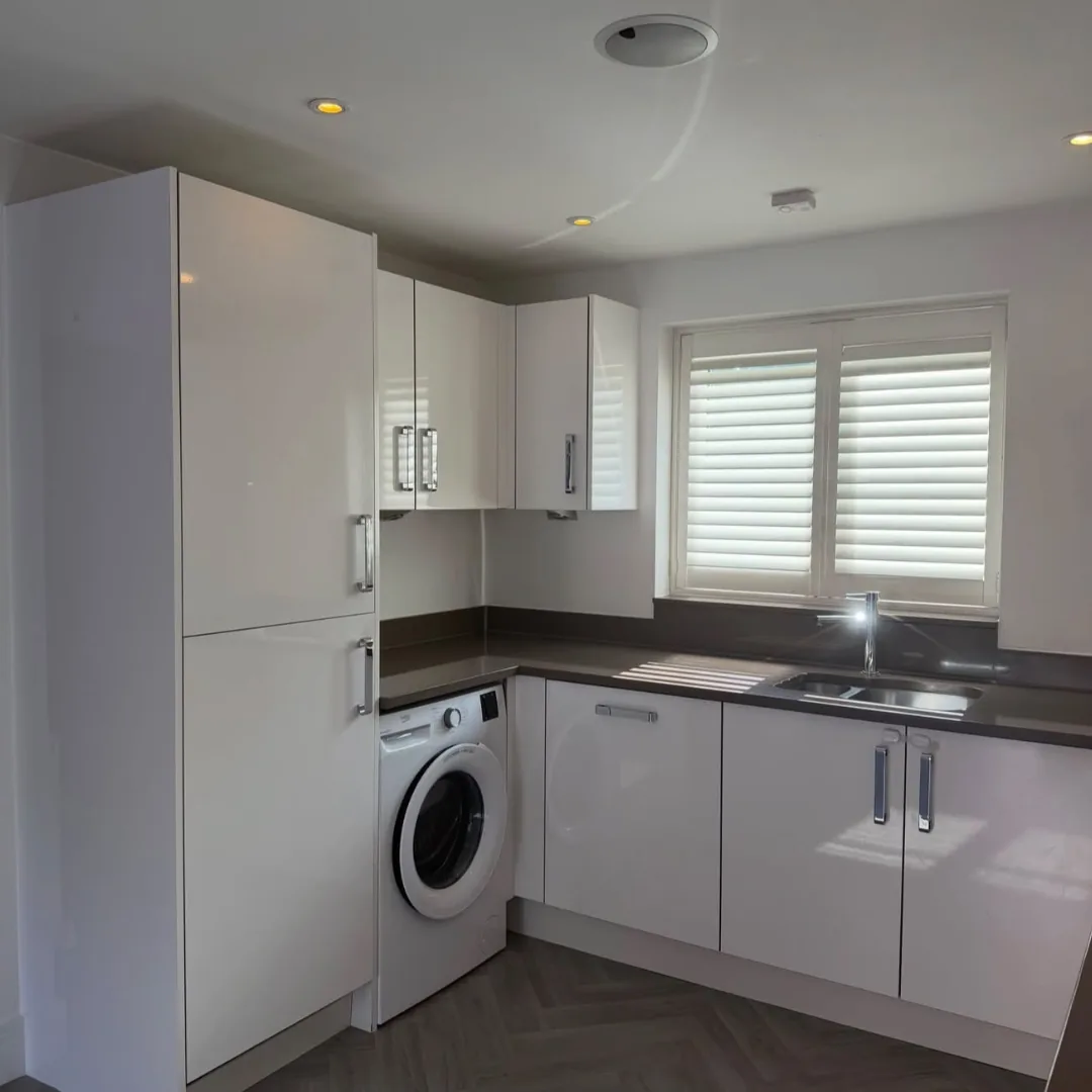 White gloss handleless kitchen cabinets with corner sink and herringbone floor