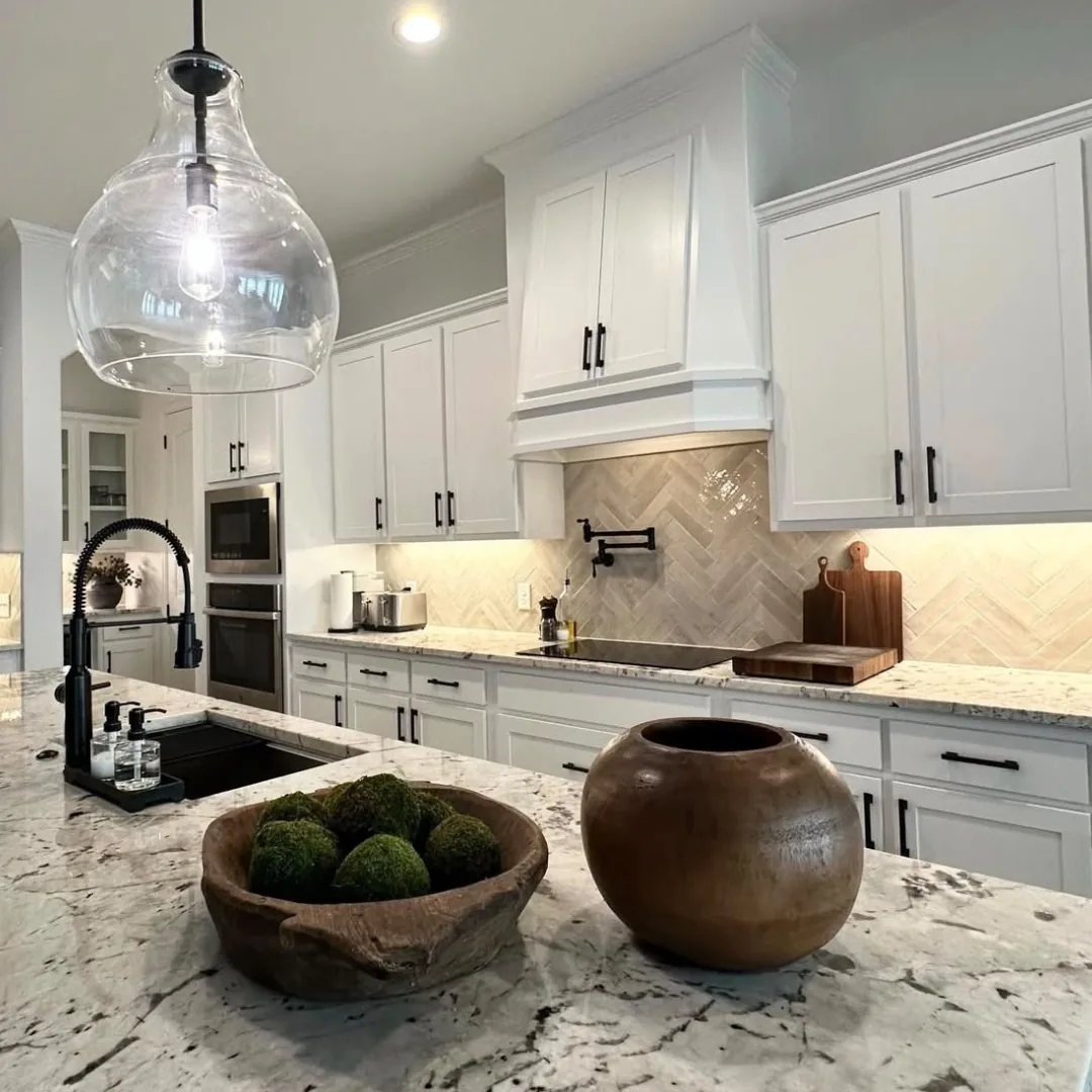 White kitchen with herringbone tile backsplash and a granite island countertop